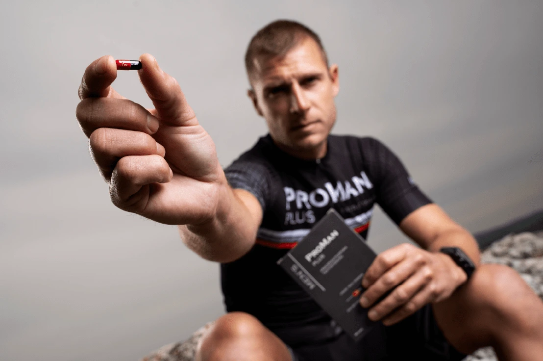 Natural Pharmaceuticals ProMan® Plus Sportowiec Michał Krysta na skale, trzymający w ręku suplement diety ProMan® Plus pokazuje kapsułkę suplementu diety ProMan® Plus.