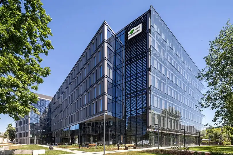 Natural Pharmaceuticals ProMan® Plus Nowoczesny szklany budynek biurowy otoczony zielenią pod błękitnym niebem.