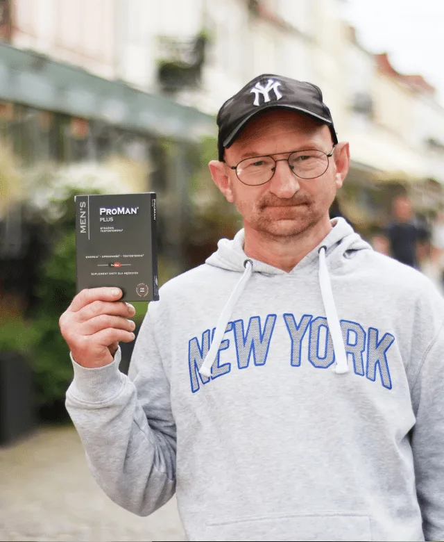 Natural Pharmaceuticals ProMan® Plus Mężczyzna w okularach i czapce z napisem NY, ubrany w szarą bluzę 