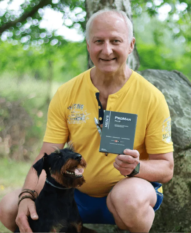 Natural Pharmaceuticals ProMan® Plus Uśmiechnięty siwy mężczyzna w żółtej koszulce, kucający w parku z psem rasy jamnik szorstkowłosy, trzymający opakowanie ProMan® Plus.